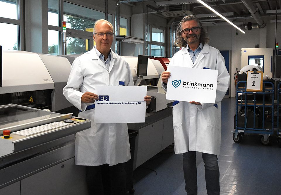 Hans Marold and Peter Brinkmann are standing in front of two machines representing the partnership